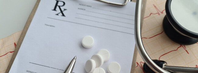Head of medical stethoscope lies on cardiogram with bunch of pills medical prescription.
