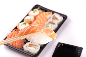 holding a piece of nigiri with chopsticks and blurred sushi tray in the background