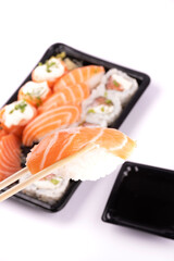 holding a piece of nigiri with chopsticks and tray of oriental food blurred in the background