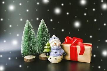 Christmas card, on a black background, a snowman with a Christmas tree in his hands, a large New Year's gift with a red bow and green Christmas trees, delicate white snowflakes.  Christmas, New Year.