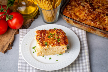 Pasta casserole bechamel sauce topped with melted mozzarella cheese and served in a white baking dish on a table (Turkish name; firinda makarna or firin makarna)