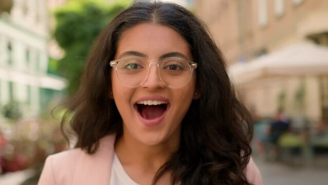 Close up portrait teen amazed excited woman Indian Arabian female girl looking at camera toothy smiling outside street town. Surprised businesswoman shouting wow success open mouth shock enjoy victory