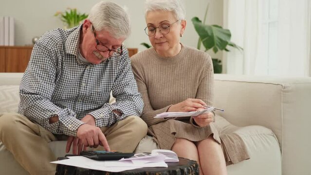 Middle Aged Senior Couple Sit With Paper Document Doing Financial Paperwork. Older Mature Man Woman Reading Paper Bill Managing Bank Finances Calculating Taxes Planning Loan Debt Pension Payment