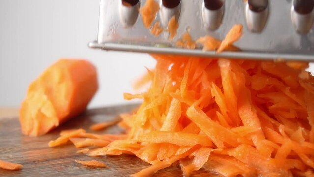 Close-up shot of a pile of grated carrots under a metal grater.