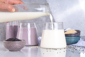 Black and white sesame milk, Alternative vegan non-dairy milk drink on glass and bottles with sesame seeds on light stone background. Raw food, vegetarian natural organic food diet