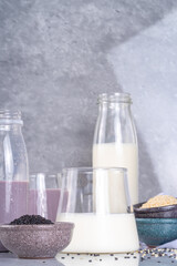 Black and white sesame milk, Alternative vegan non-dairy milk drink on glass and bottles with sesame seeds on light stone background. Raw food, vegetarian natural organic food diet