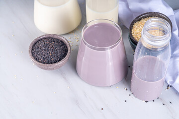 Black and white sesame milk, Alternative vegan non-dairy milk drink on glass and bottles with sesame seeds on light stone background. Raw food, vegetarian natural organic food diet