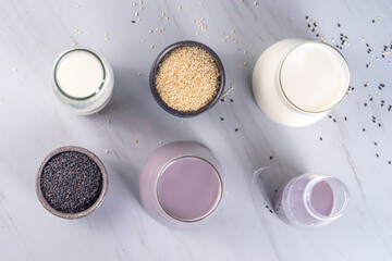 Black and white sesame milk, Alternative vegan non-dairy milk drink on glass and bottles with sesame seeds on light stone background. Raw food, vegetarian natural organic food diet