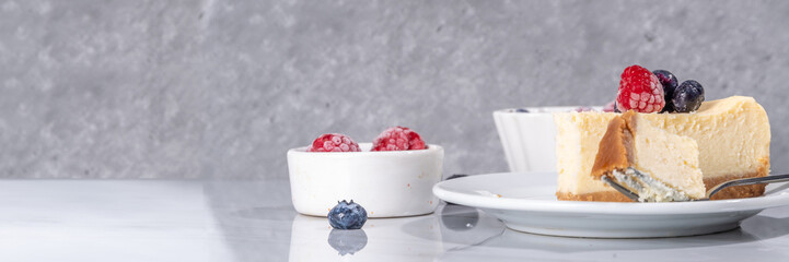 Cheesecake portion slice on plate, with raspberry on blueberry on white marble background 
