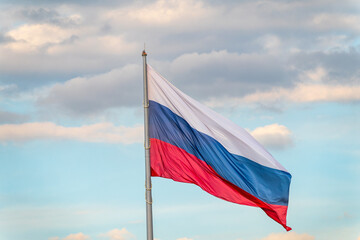 Russian tricolor flag waving in the wind against a blue sky.