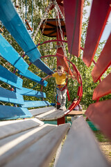Smiling teenage boy goes through a hanging wooden tunnel. The boy has fun in the rope par