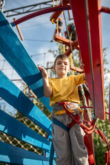 Smiling teenage boy goes through a hanging wooden tunnel. The boy has fun in the rope par