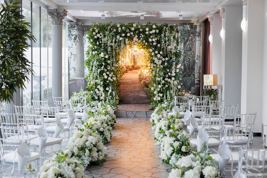 Wedding ceremony. A beautiful and stylish wedding arch, decorated by various fresh white flowers with white chairs, standing. Celebration day.