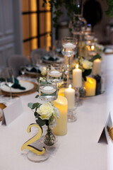 Wedding decorations. Served wedding table with decorative fresh white flowers, candles. Celebration details. Flower composition roses, plates, candles in candlesticks and green napkins