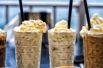 Two or three chocolate-flavored milkshakes with a cup of coffee next to them.