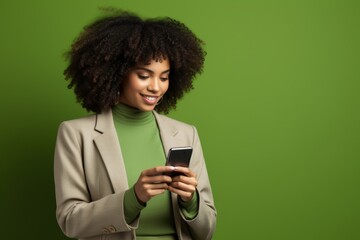 Fototapeta na wymiar Portrait of a happy black woman using a smartphone on a green studio wall. Amazing app.