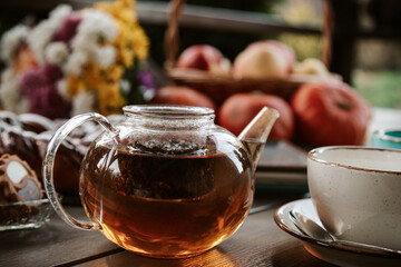 Black tea in a glass teapot on wooden table with fall decor