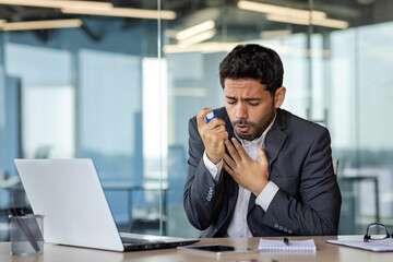 Arab businessman suffering from asthma in modern office, young man holding inhaler in hand and holding chest, breathing hard, breathing and health problems