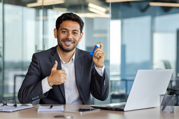 Satisfied arab businessman sitting in bright office holding oxygen inhaler for asthma in hands, giving thumbs up, health concept, smiling and looking at camera.