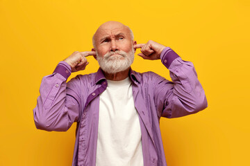 offended old bald grandfather in purple shirt covers his ears with his hands and ignores on yellow...