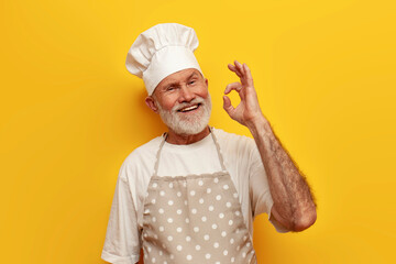 old bald grandfather chef in apron and hat smiles and shows ok symbol on yellow isolated background