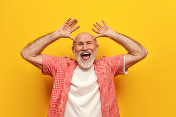 joyful old grandfather in summer shirt fooling around and making faces on yellow isolated background - obrazy, fototapety, plakaty