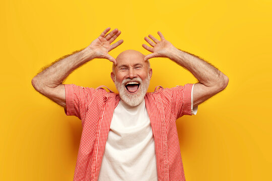 joyful old grandfather in summer shirt fooling around and making faces on yellow isolated background