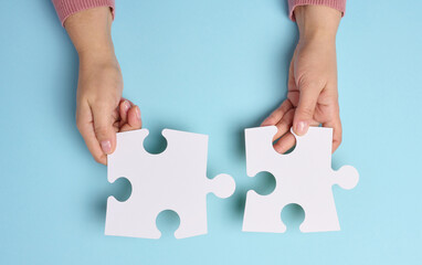 Female hand holds two large paper empty white jigsaw puzzles on a blue background