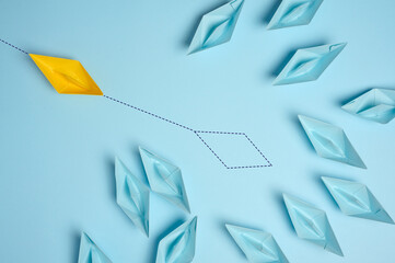 Group of blue paper boats and one red with paths on a blue background. Concept of a strong leader...