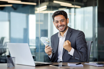 Fototapeta na wymiar Surprised happy man businessman sitting in modern office at table in front of laptop, happy with huge win, online earnings, smiling and looking at camera.