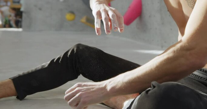 Slow motion closeup of a fit young man taping up his chalked hands and fingers during a climbing session in a bouldering gym