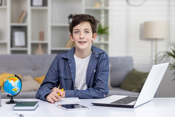 Portrait of happy teenage boy student sitting at table at home, studying via distance learning, doing homework, smiling, looking at camera. - Powered by Adobe