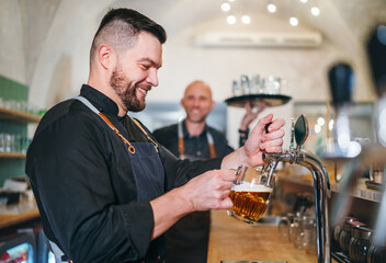 Stylish bearded barman dressed black uniform beer tapping at bar counter and waiter with tray...