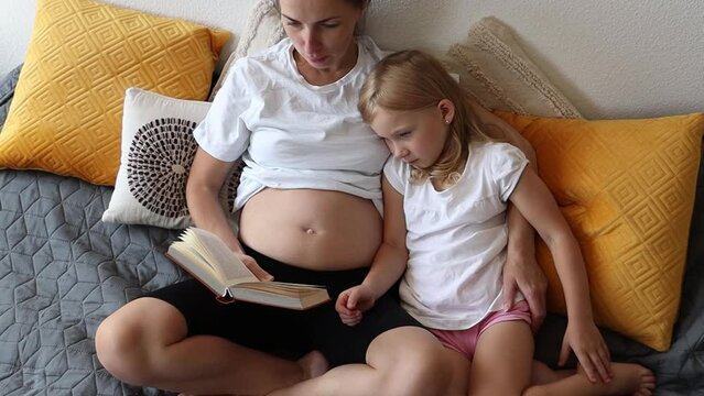 Pregnant mother and little daughter reading a book.