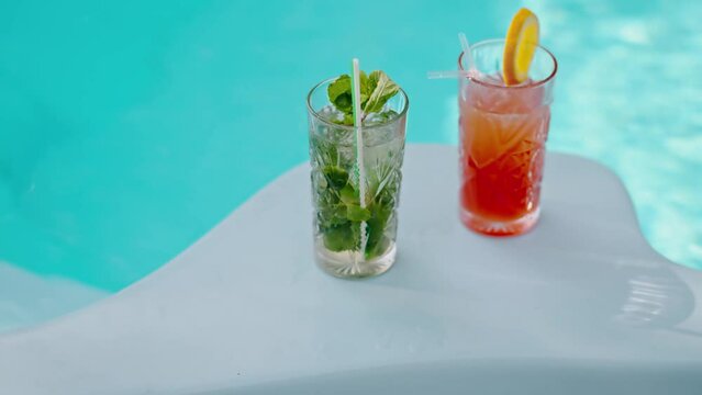 Glasses with alcohol cocktails standing on corner poolside. Pool party with alco drinks. Friends ordered mojito and aperol in summer. New bartender menu. Cold cocktails