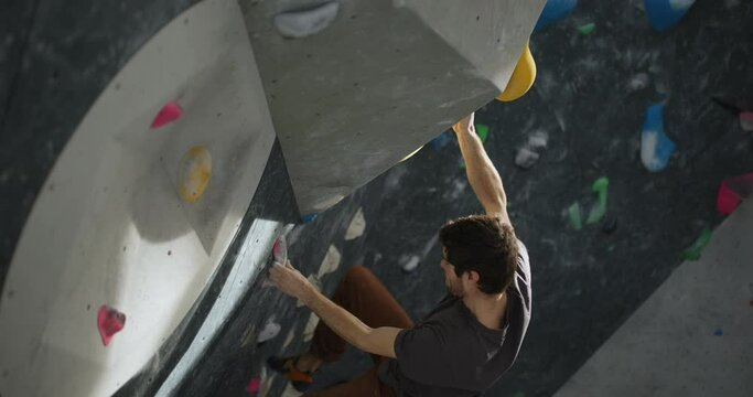 Fit young man using handholds to climb up an artificial wall in a bouldering gym