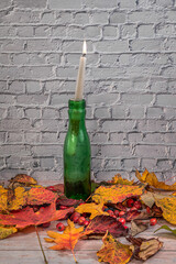 Green bottle and candle white brick wall autumn color leafs