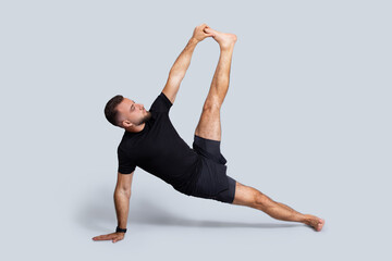 Naklejka premium Serious millennial caucasian man in sportswear practice yoga, stretching leg