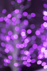 Christmas lilac glowing background. Lilac festive abstract shiny defocused background with flashing garlands. Tinsel blurred gold bokeh on a black background.