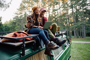 Happy couple using digital tablet while camping in woods.