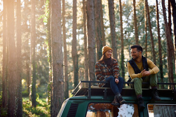Happy couple talks while sitting on roof of their camper van in woods. © Drazen