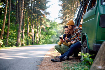 Young couple of campers using mobile phone while traveling with their van in nature.
