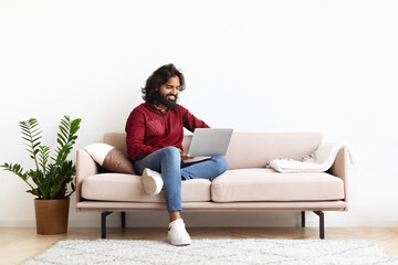 Smiling Indian Man Sitting On The Couch Working On Laptop