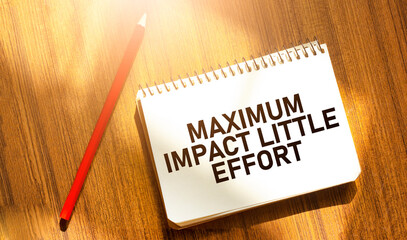 MAXIMUM IMPACT LITTLE EFFORT on notebook with red pencil on wooden background