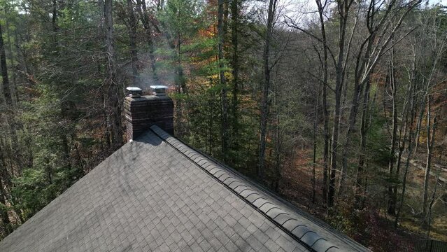 smoke coming from chimey of a suburban home in the woods (rural house drone footage shot from above) shingles, roofing, fireplace exhaust, country home, rustic luxury architecture