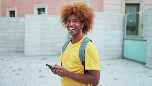 Portrait of a young African American student using a mobile phone looking at the camera smiling. Slow motion video of young multiethnic student boy looking at camera smiling while using mobile phone.