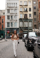 Pretty young woman with long brown hair  and white pants walking in the streets of Manhattan