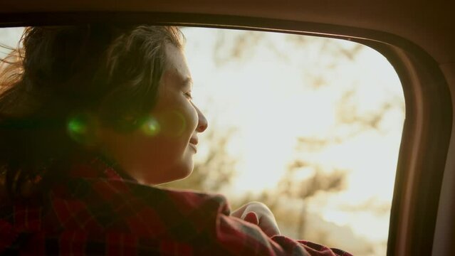 School age girl smiling carelessly and enjoying journey. Happy family travel concept. Child leaned out of car window smiling with pleasure
