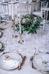 The wedding festive table is decorated with floral arrangements, glasses, plates and cutlery, the table is covered with a beautiful tablecloth