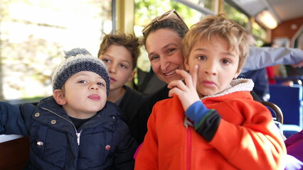 Mother and children riding train going to the mountains, Mom surrounded by small boys traveling in transportation looking at camera posing and smiling - Powered by Adobe